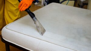 Technician cleaning a stained mattress with a professional steam cleaning machine, showing a clear contrast between the cleaned and uncleaned sections